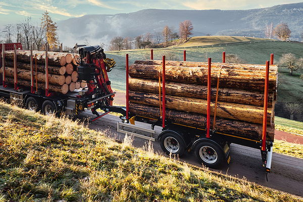 LKW mit Zentralachsanhänger von DOLL fährt im Morgengrauen über eine schmale Landstraße zwischen Wiesen und Feldern